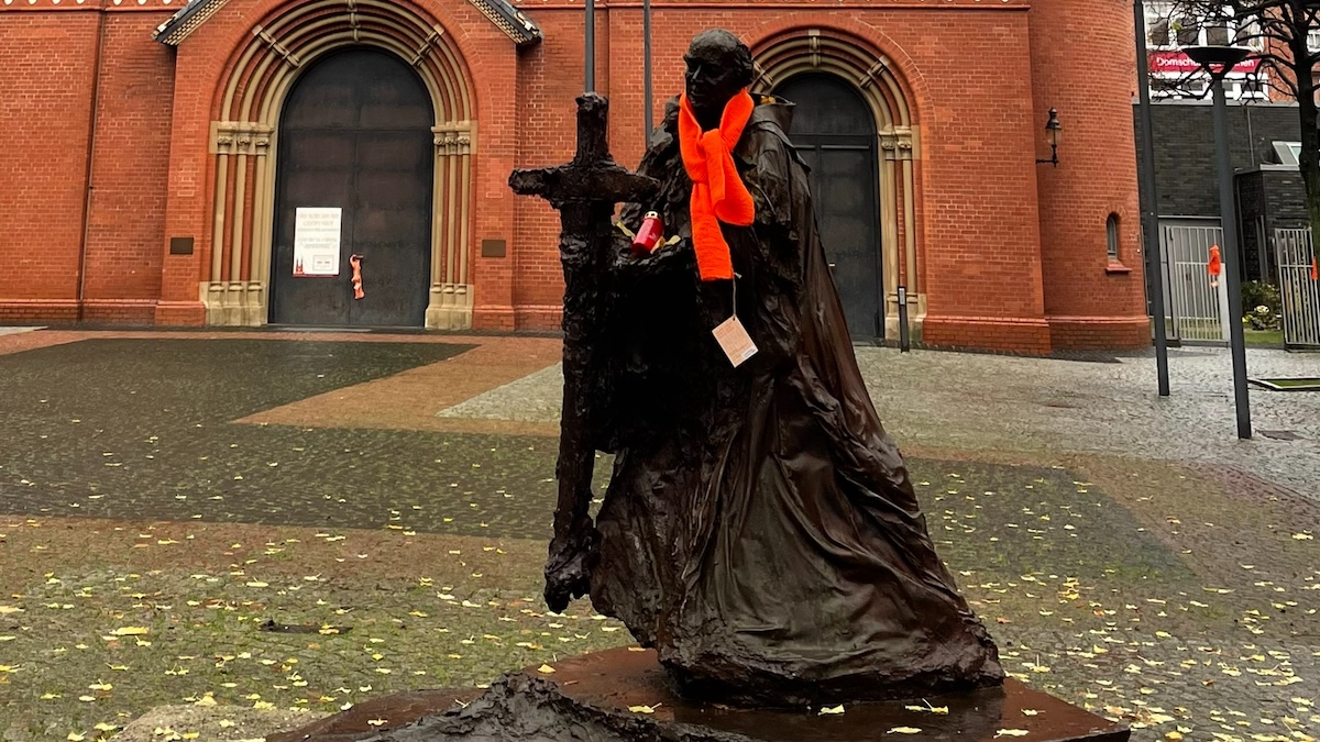 Das Bild zeigt den heiligen Ansgar als fast lebensgroße Statue aus Metall - mit einem orangefarbenen Schal.